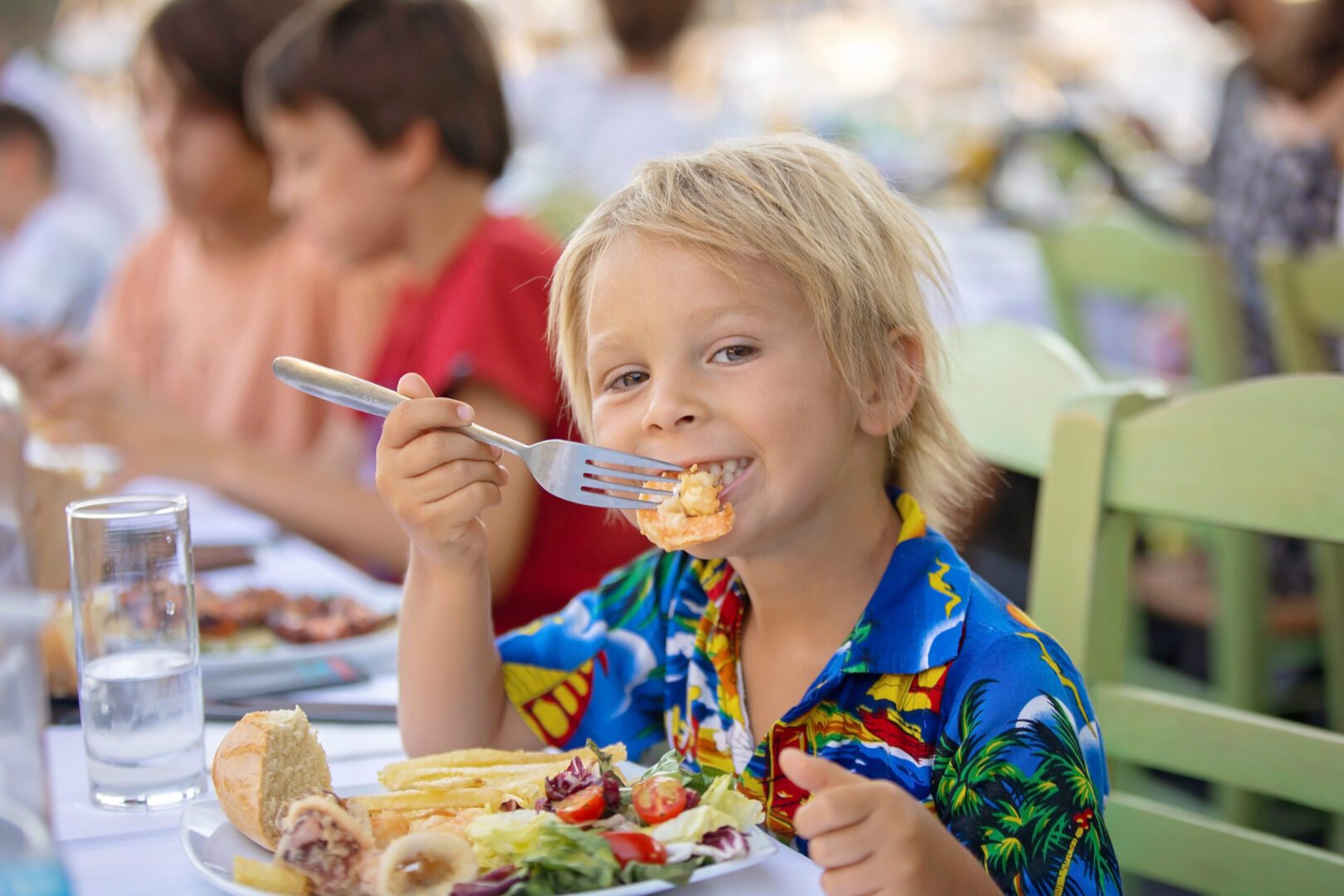 Smiling child enjoys a colorful meal at a lively outdoor setting.