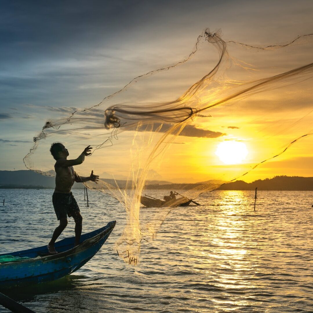 Fisherman casting a net at sunset on a calm sea.
